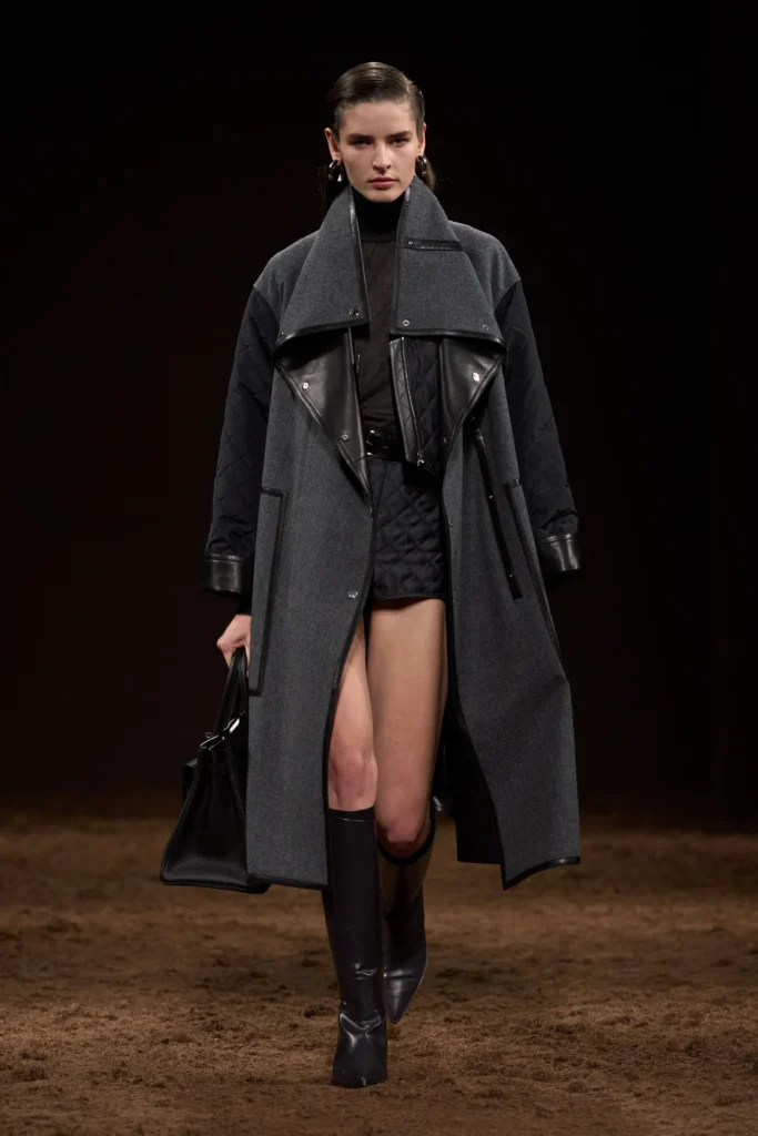 Street-style photo of a woman crossing the street in black knee-high leather boots paired with a cream mini skirt and a black quilted handbag. The warm lighting and natural movement capture effortless fall elegance and quiet luxury appeal.
