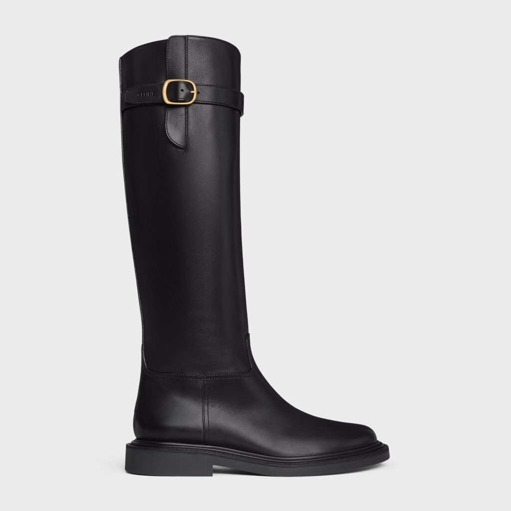 Street-style photo of a woman crossing the street in black knee-high leather boots paired with a cream mini skirt and a black quilted handbag. The warm lighting and natural movement capture effortless fall elegance and quiet luxury appeal.